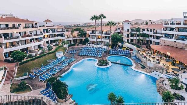 Un resort con una amplia piscina central, varios balcones y vistas al paisaje circundante.