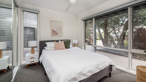 A bedroom with a large bed, two bedside tables with lamps, a window with a view of trees, and a ceiling fan. - Gawalla Escape with Pool in Rye (Rye)