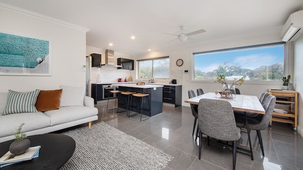 A modern kitchen with a central island, a dining area with a table and chairs, and a living room with a sofa and coffee table. - Gawalla Escape with Pool in Rye (Rye)