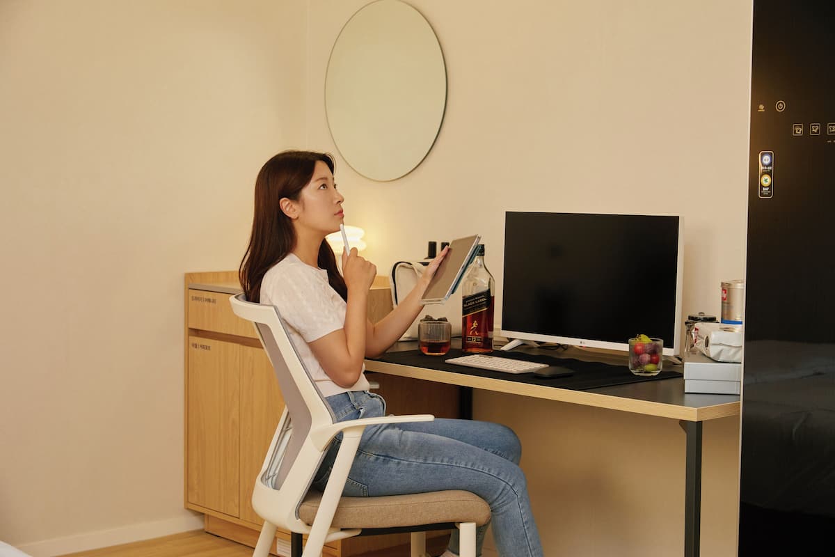 Iemand zit aan een bureau met een computer, een lamp en een fles water.