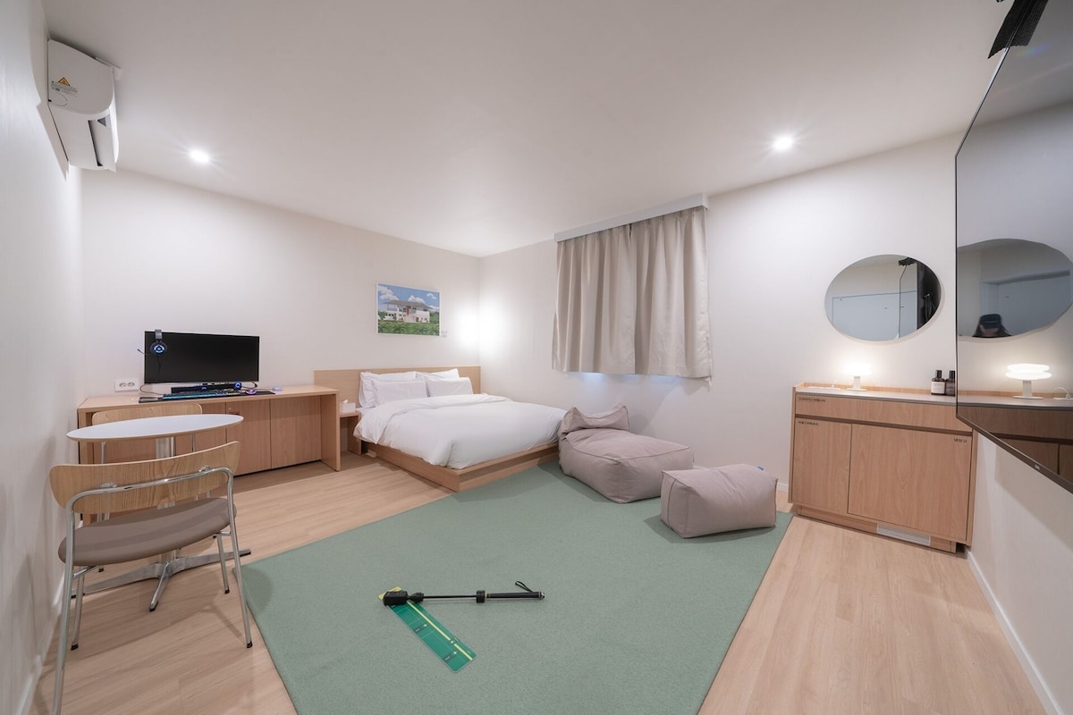 Ein modernes Hotelzimmer mit Bett, Schreibtisch, Fernseher, Spiegel und einer grünen Yogamatte.
