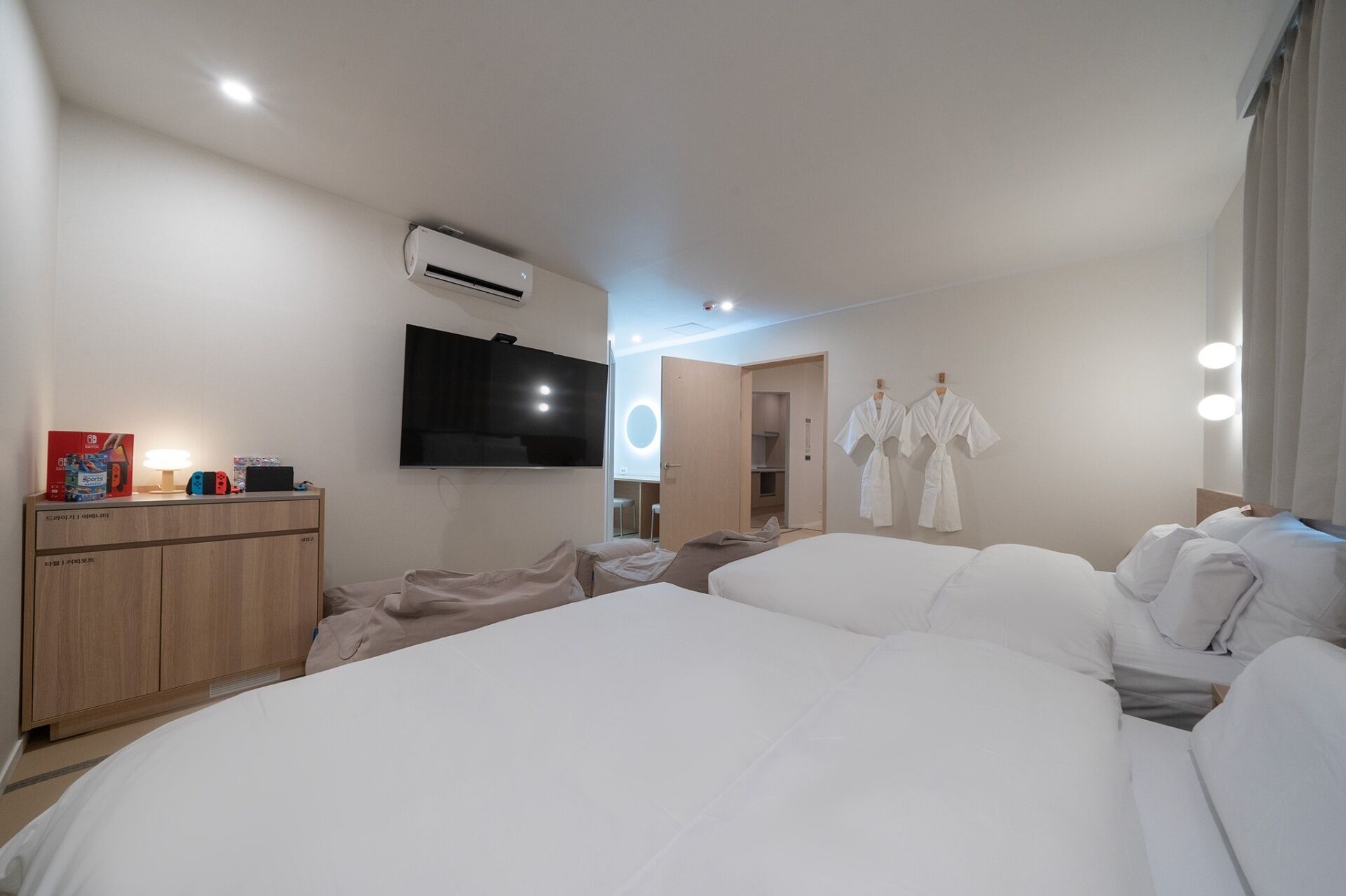 A hotel room with a large bed, a TV mounted on the wall, an air conditioning unit, a wardrobe, and a mirror with lights.