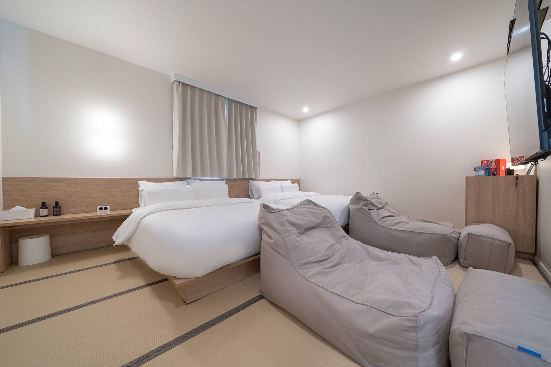 Camera d'albergo con due letti, un divano, un comodino, una lampada e una televisione.