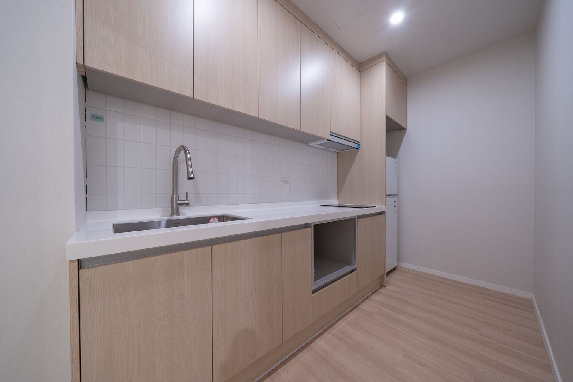 A modern kitchen with light wood cabinets, a stainless steel sink, and a built-in oven.