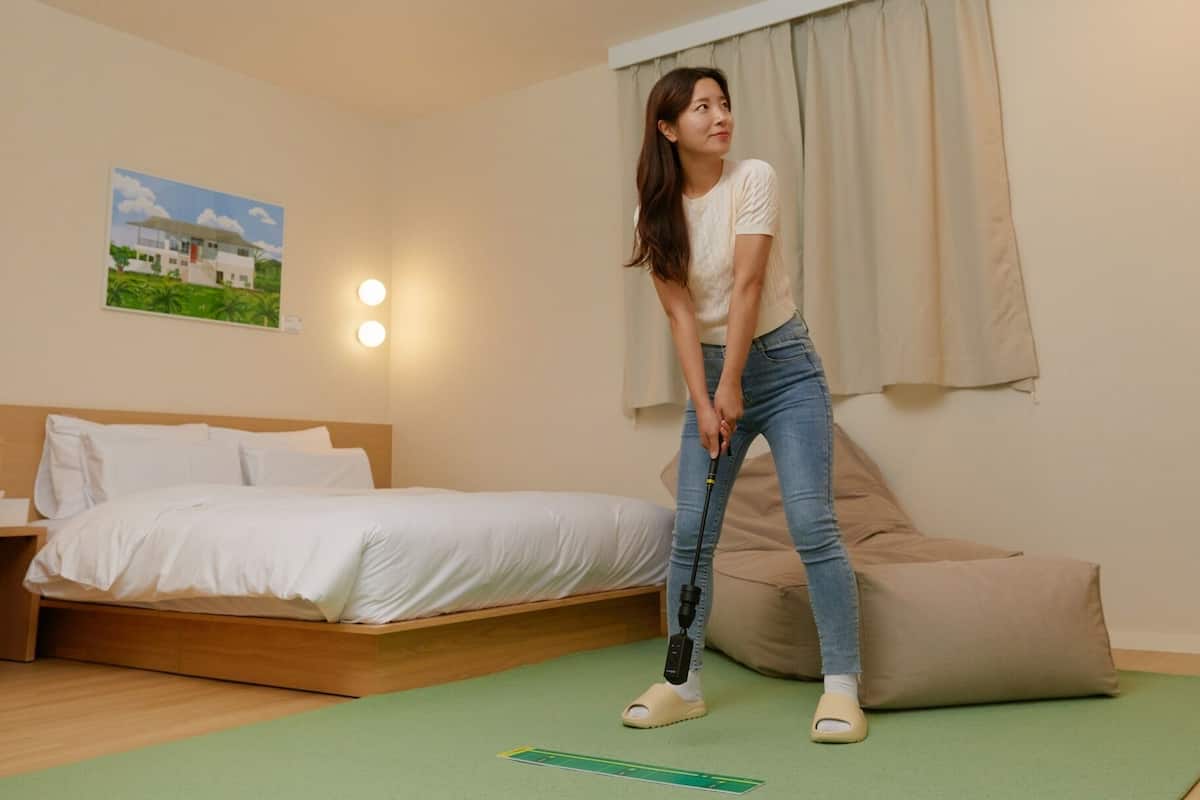 Een hotelkamer met een bed, een nachtkastje, een groene mat en een schilderij aan de muur.