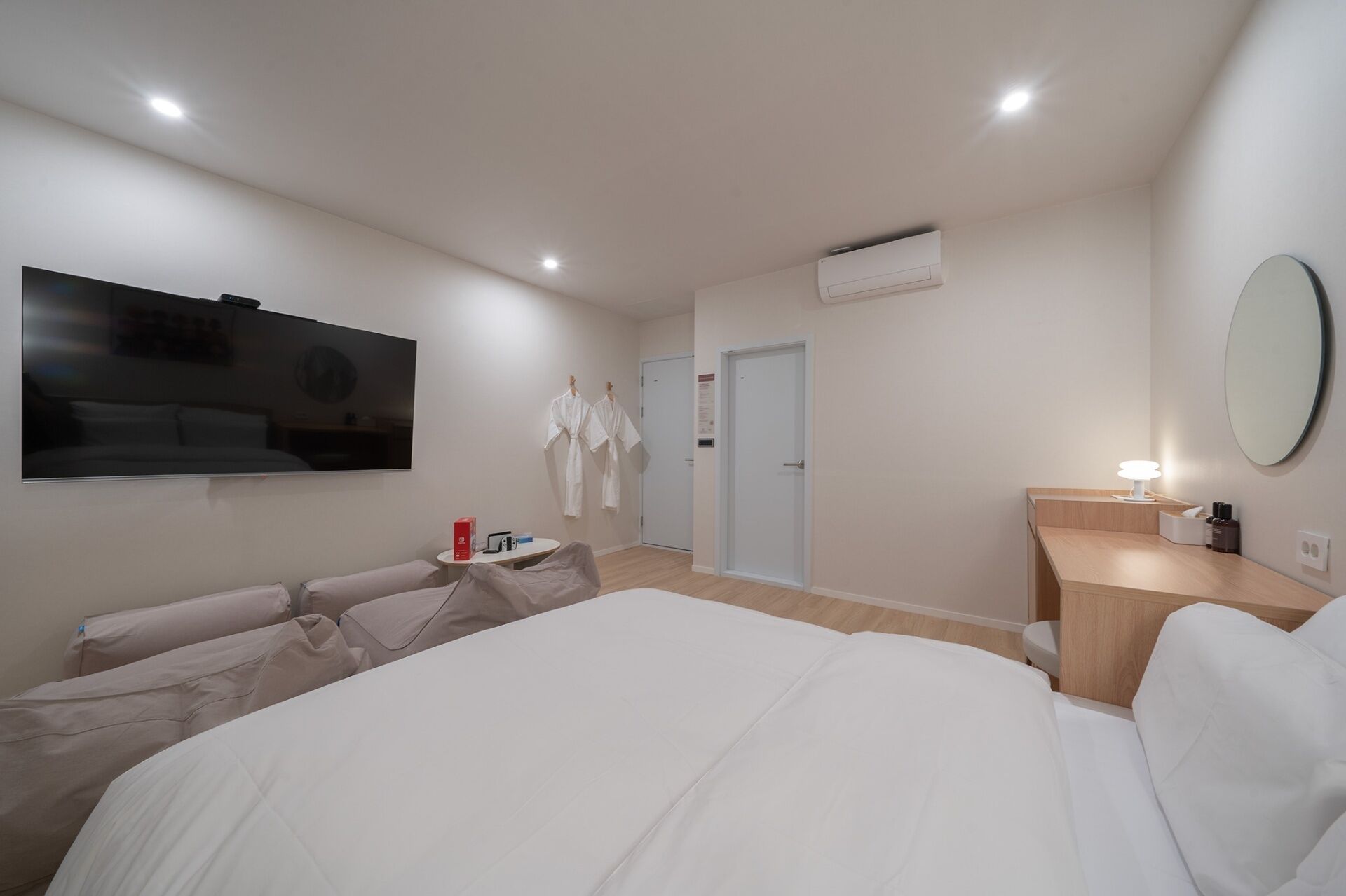 Habitación de hotel moderna con una cama grande, un televisor de pantalla plana montado en la pared, una mesita de noche con lámpara y un espejo.