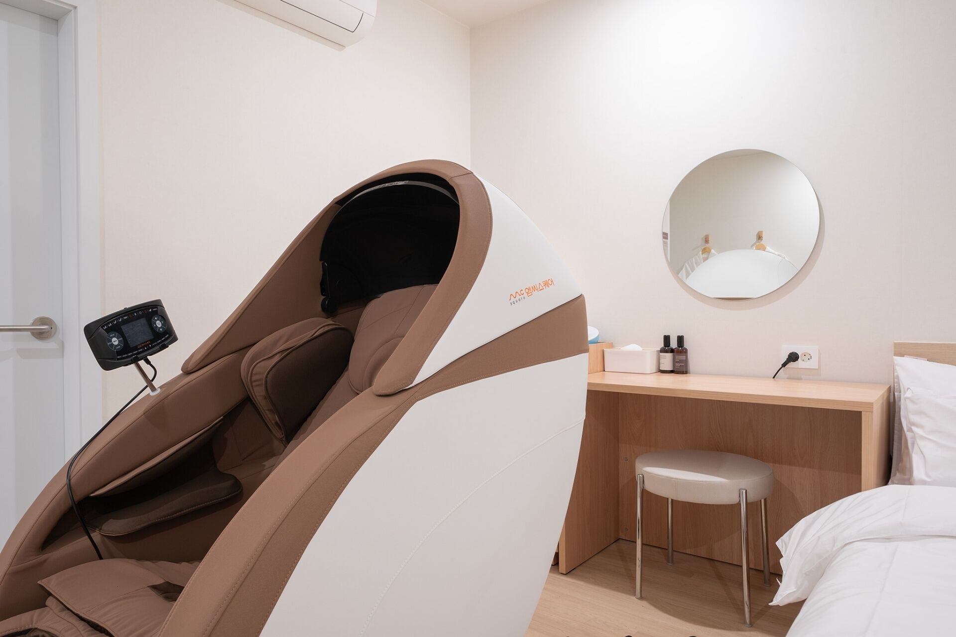 Una habitación moderna con sillón de masajes, un escritorio pequeño con espejo y una cama.