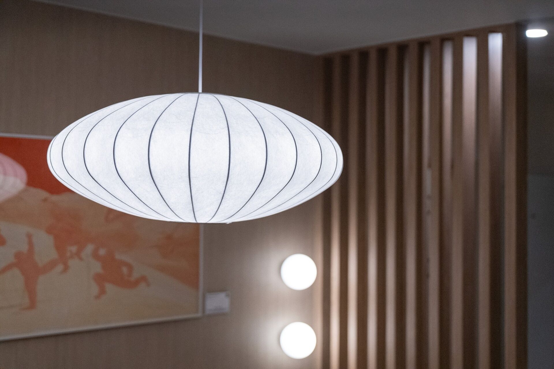 A hanging light fixture with a white, circular design and a wooden slat wall in the background.