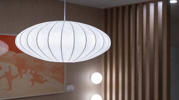 A hanging light fixture with a white, circular design and a wooden slat wall in the background.