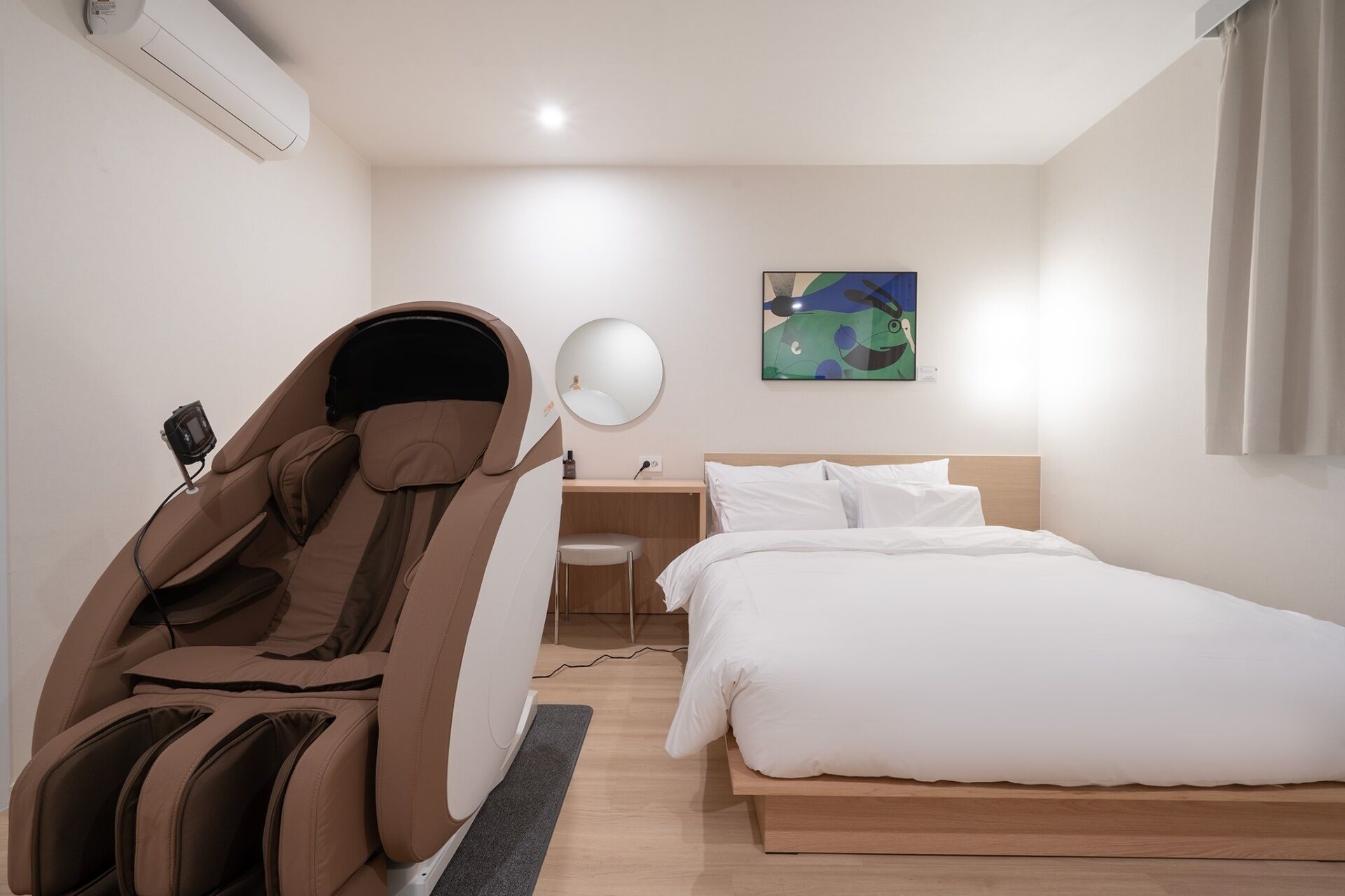 Habitación de hotel con una silla de masajes, una cama, un escritorio y un cuadro en la pared.