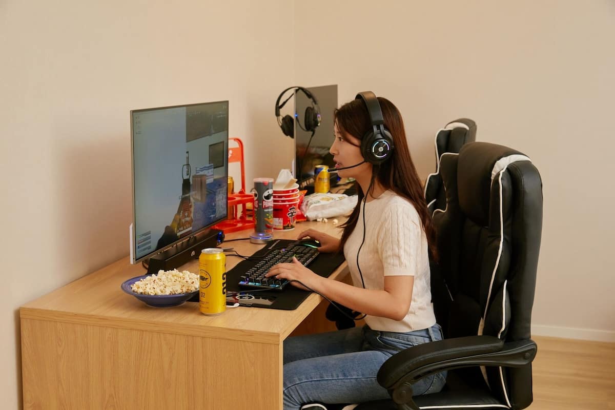 Een persoon zit aan een bureau met een computer, een hoofdtelefoon en een schaal popcorn.