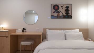 Habitación de hotel con cama, escritorio, silla, espejo redondo y una obra de arte colgada en la pared.