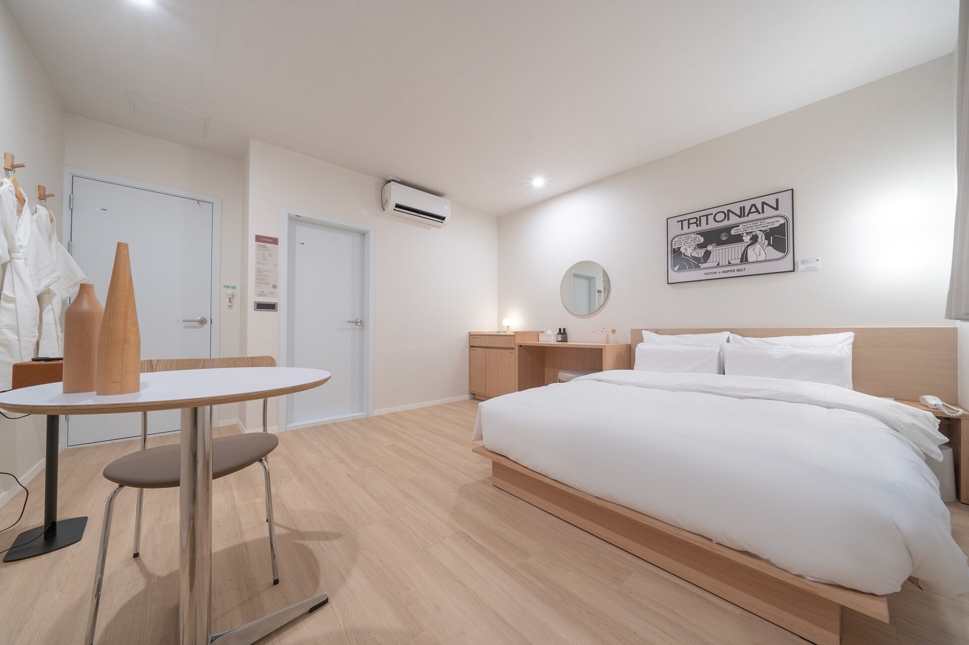 Una habitación de hotel con una cama, mesita de noche y un escritorio con una silla. Hay un espejo en la pared y un cuadro enmarcado sobre la cama.