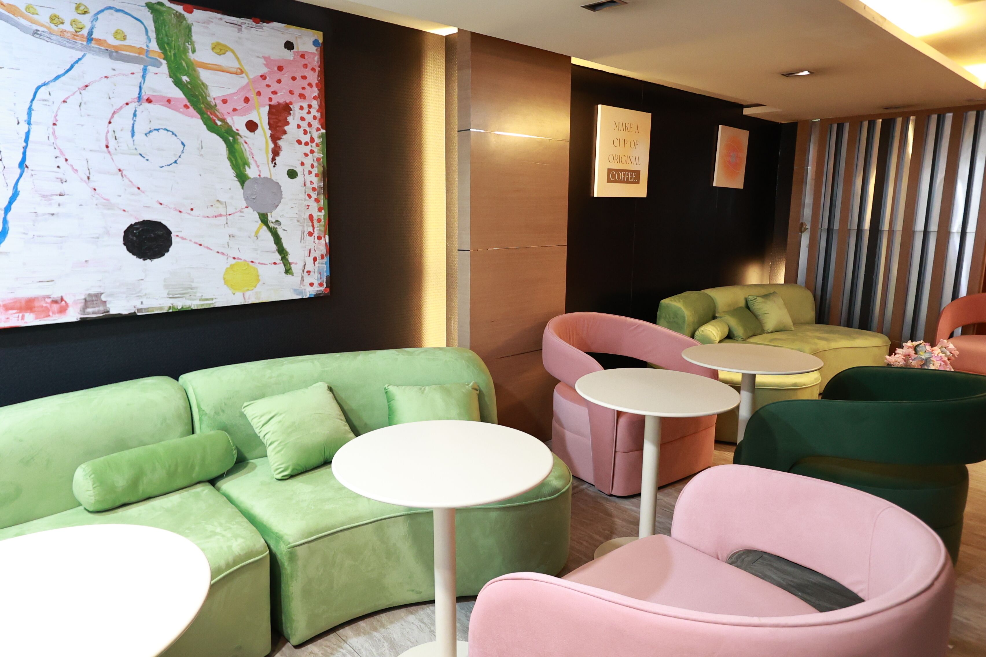 A modern lounge area with a green sofa, pink chairs, and small round tables.