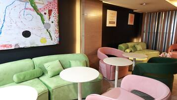 A modern lounge area with a green sofa, pink chairs, and small round tables.