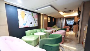 A modern lounge area with green and pink seating, a large abstract painting, and a view into the kitchen area. - Metacity MK (Kowloon)