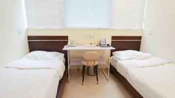 A room with two single beds, a desk with a chair, a telephone, a kettle, and a small table.
