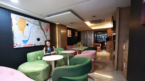 A modern lounge area with green and pink seating, a large abstract painting on the wall, and a well-lit interior. - Metacity MK (Kowloon)