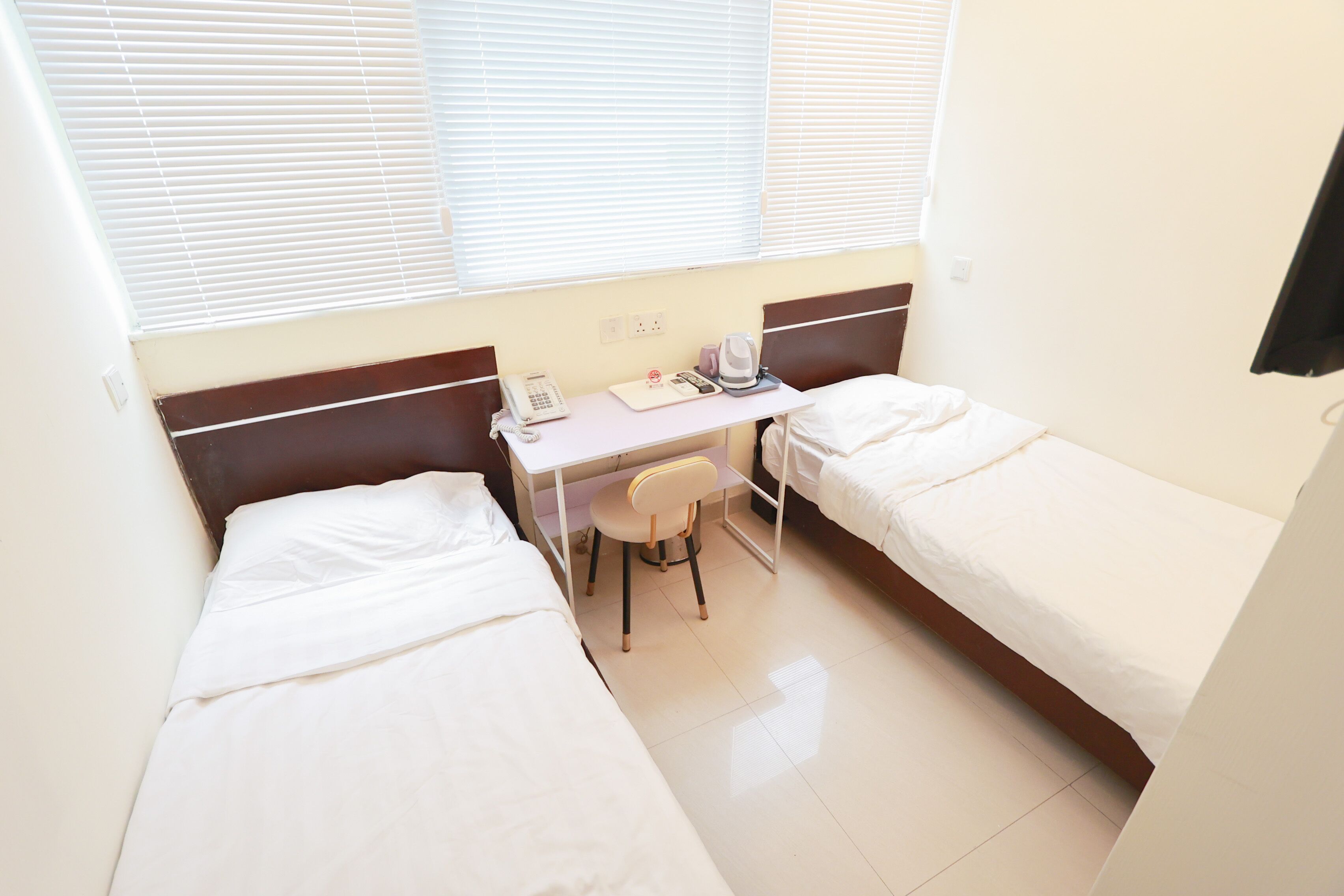 Une petite chambre propre, équipée de deux lits simples, d’un bureau avec une chaise, d’un téléphone et d’une bouilloire.