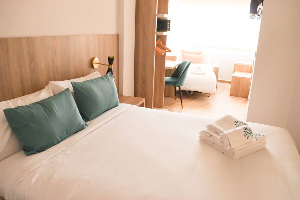 A hotel room with a bed, pillows, a chair, a desk, and a mirror.
