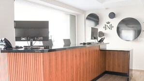 Un mostrador de recepción con detalles de madera, un espejo grande y un letrero fijado a la pared con un símbolo de corona.