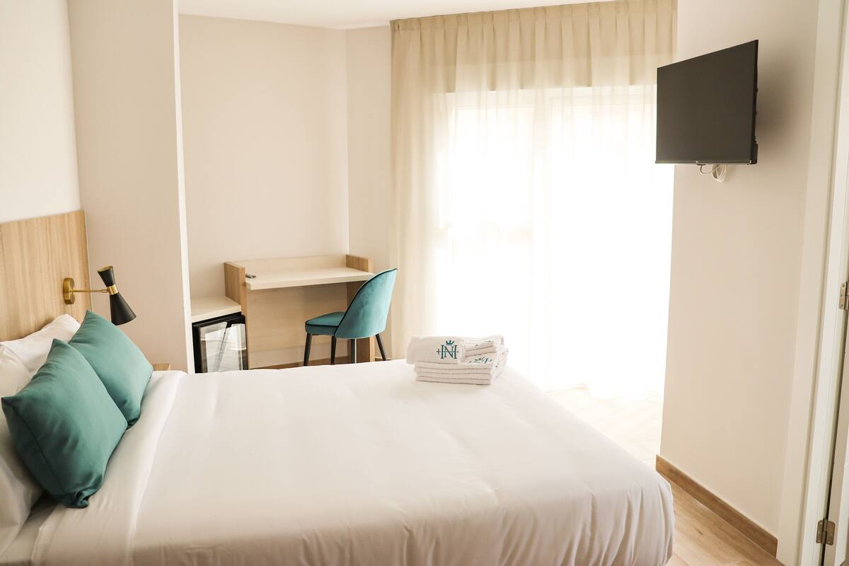 A hotel room with a bed, a desk, a chair, a TV, and a window with curtains.