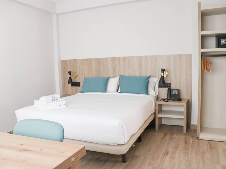 A hotel room with a bed, bedside tables, a desk, and a wardrobe.