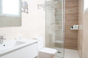 Un baño moderno con ducha de vidrio, lavamanos blanco y retrete.