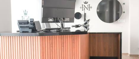A reception desk with a flat-screen monitor, a cash register, and a printer. There are wall decorations including a crown symbol and circular designs.