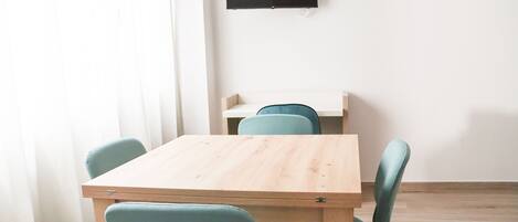 A room with a wooden table and four chairs, a flat-screen TV mounted on the wall, and an air conditioning unit.
