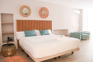 A neatly arranged bedroom with a wooden headboard, a bed with white and teal bedding, two wall mirrors, a bedside table with a lamp, and a small seating area with a chair and table. - Hotel Narcea Santa Pola (Santa Pola)