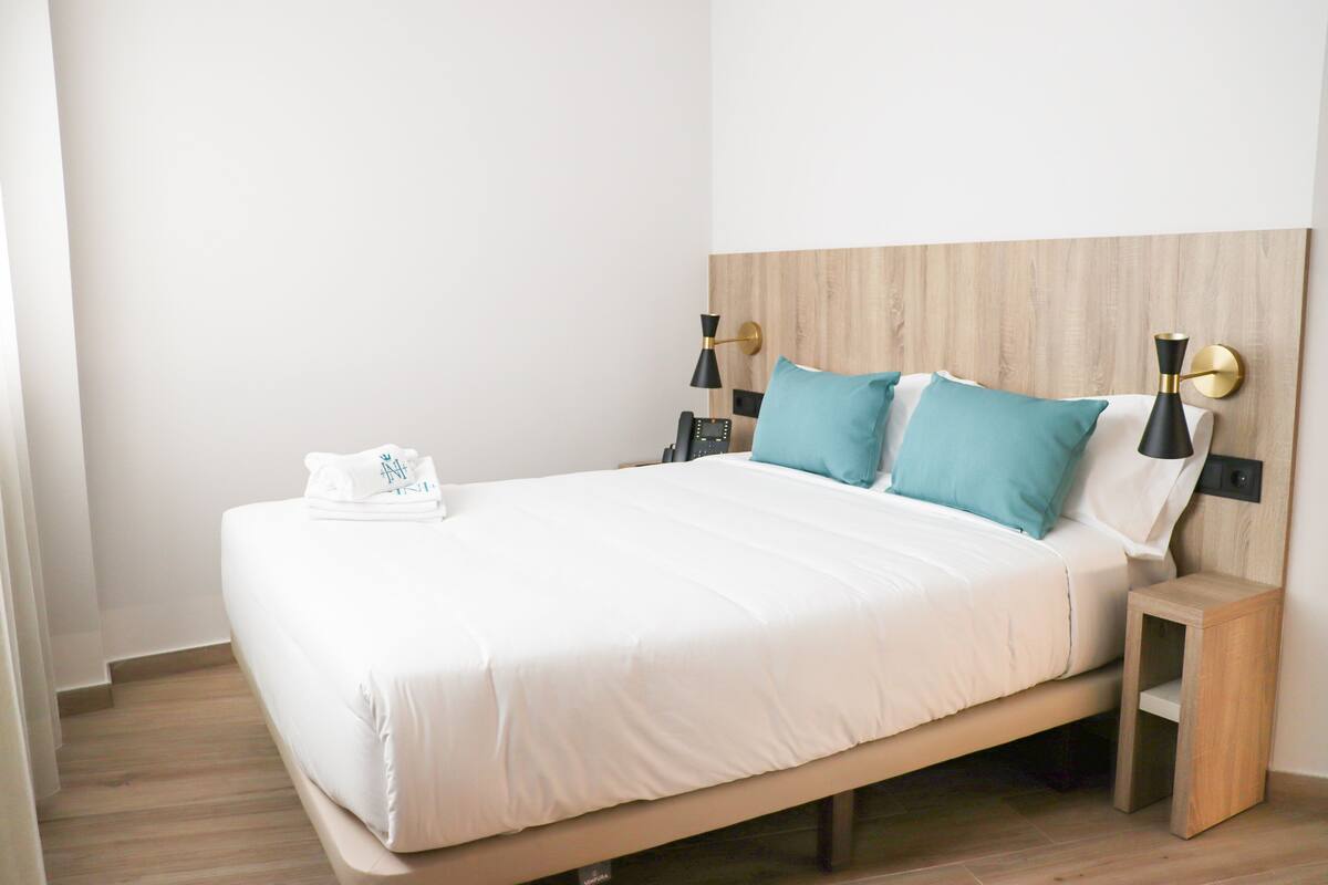 A neatly made bed with white linens, two bedside tables with lamps, and a wooden headboard.