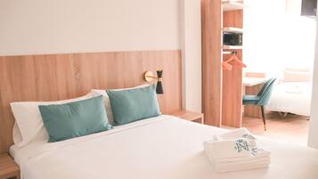 Una cama bien hecha con dos almohadas, una mesita de noche, una lámpara de pared, un armario de madera y una silla.