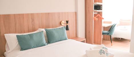 A neatly made bed with two pillows, a bedside table, a wall-mounted lamp, a wooden wardrobe, and a chair.