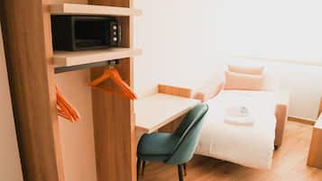 Una habitación de hotel compacta con una cama, un escritorio, una silla, un microondas y un armario.