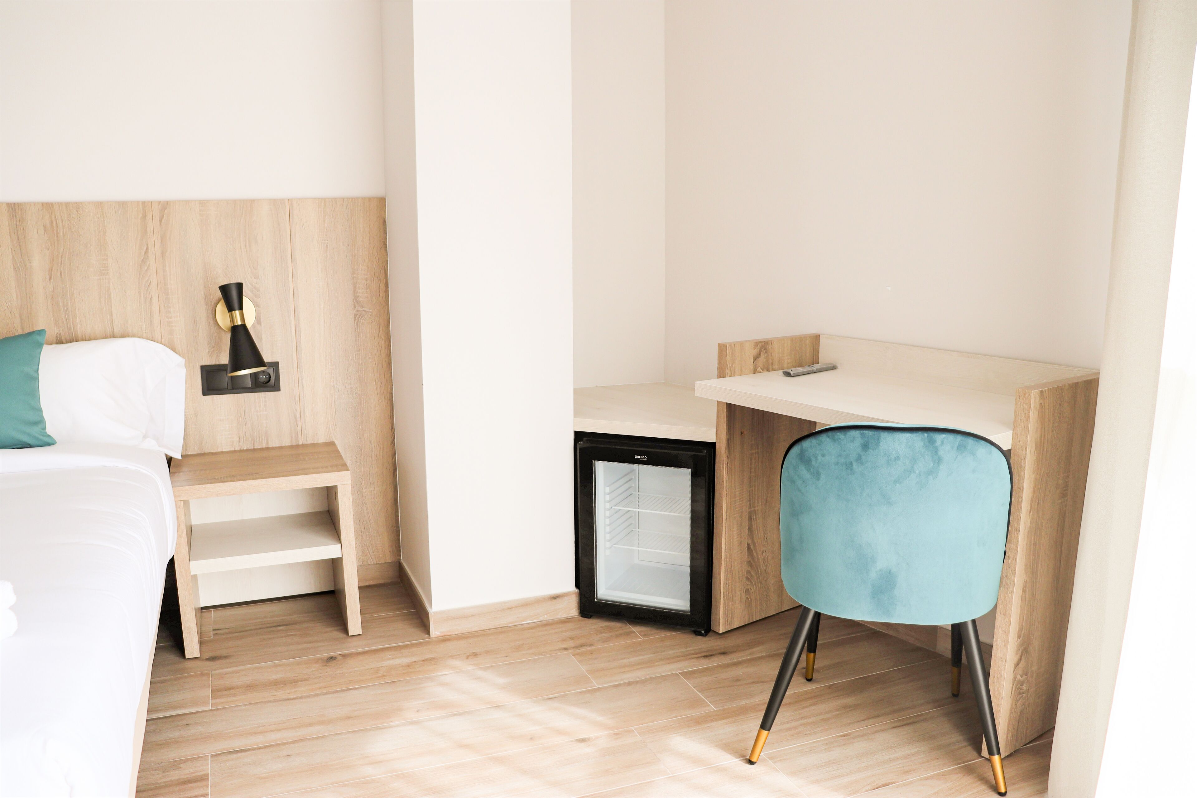 A hotel room with a bed, a desk, a chair, a small refrigerator, and a nightstand.