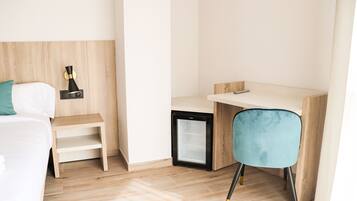 A hotel room with a bed, a desk, a chair, a small refrigerator, and a nightstand.