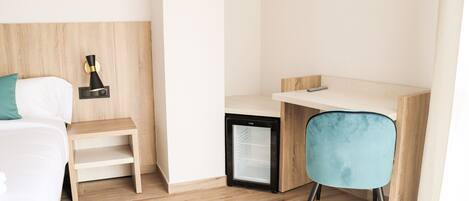 A hotel room with a bed, a desk, a chair, a small refrigerator, and a nightstand.