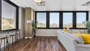 A modern living room with a large window, a sofa, a coffee table, and a bar area with stools.
