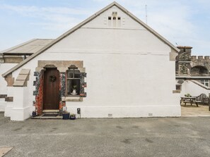 A white building with a triangular roof, a wooden door, and a small window with a wreath.