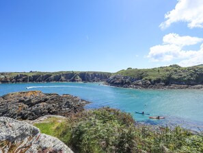 A coastal landscape with rocky terrain, clear blue waters, and a kayaker.
