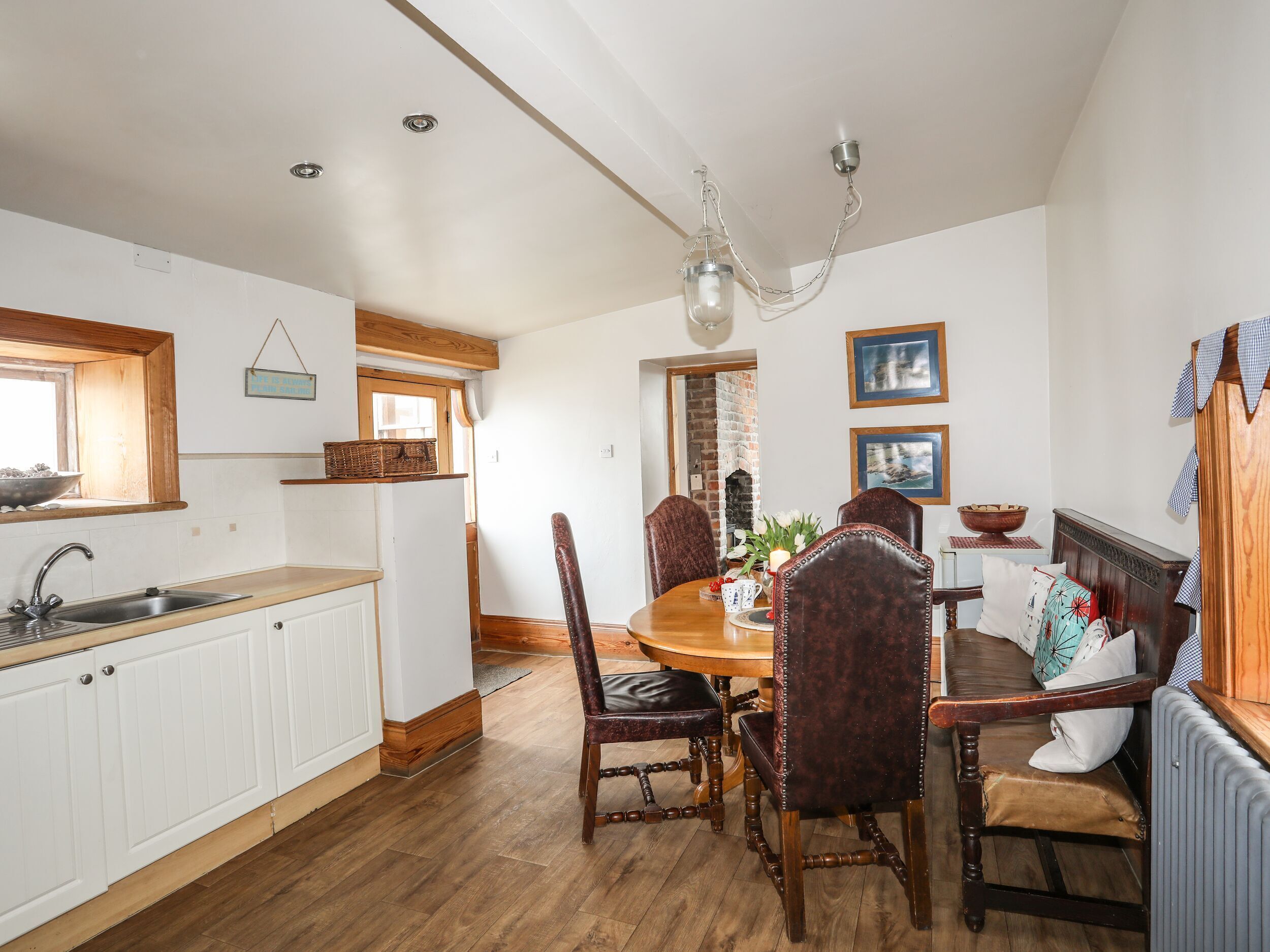 A kitchen with wooden cabinets, a dining table with chairs, a hanging light fixture, and a brick fireplace.