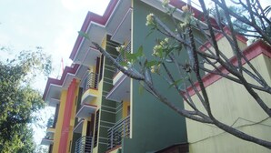 A multi-story building with balconies and a tree with flowers in the foreground. - OYO Life 90646 Villa Karsinem Pasuruan (Prigen)