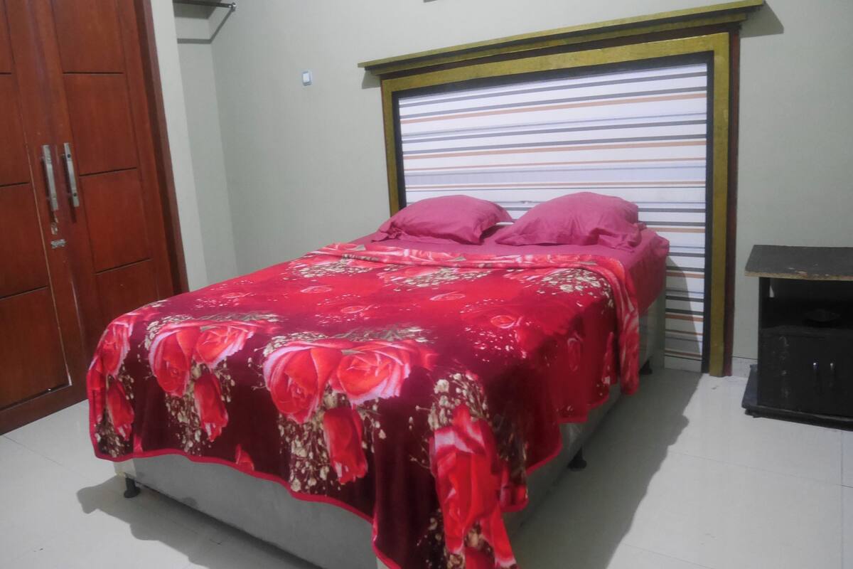 A bedroom with a bed, a wardrobe, and a window with blinds.