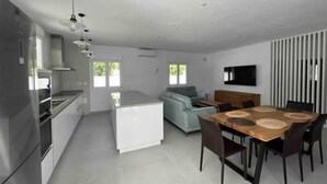 Une cuisine moderne dotée d’un îlot central, un coin repas avec une table et des chaises en bois, et un espace de vie avec un canapé et un téléviseur.