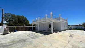 Un bâtiment moderne de couleur blanche, doté d’un patio couvert, de grandes fenêtres et surplombé d’un ciel bleu clair.