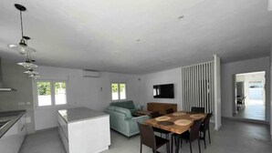 Une cuisine moderne avec un îlot central, un coin repas avec une table et des chaises en bois, un canapé bleu clair et un téléviseur fixé au mur.
