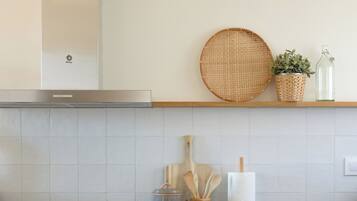 Cocina moderna con encimera negra, armarios blancos, lámpara de techo tejida y una mesa de comedor de madera con una revista.