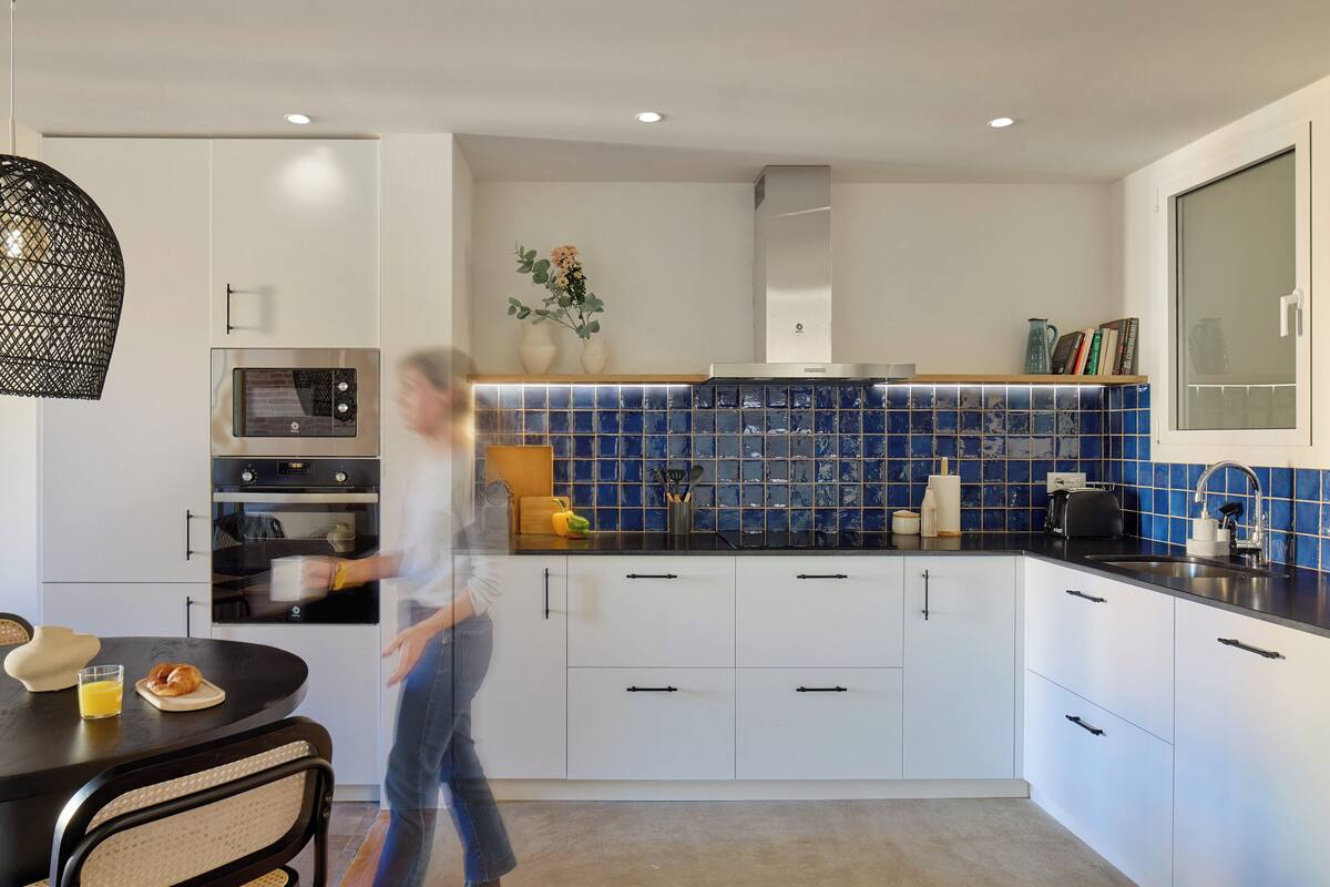 A modern kitchen with white cabinets, a blue tiled backsplash, and a black countertop.