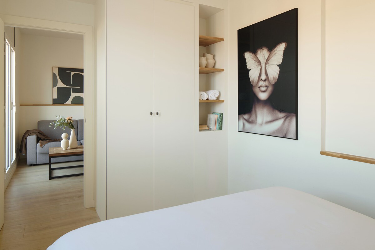 A bedroom with a bed, a wardrobe, a shelf with books, and a painting on the wall.